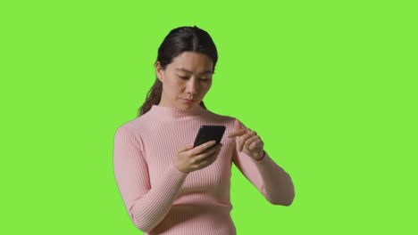 Studio-Shot-Of-Woman-Scrolling-Through-Messages-Or-Content-On-Mobile-Phone-In-Front-Of-Green-Screen-1